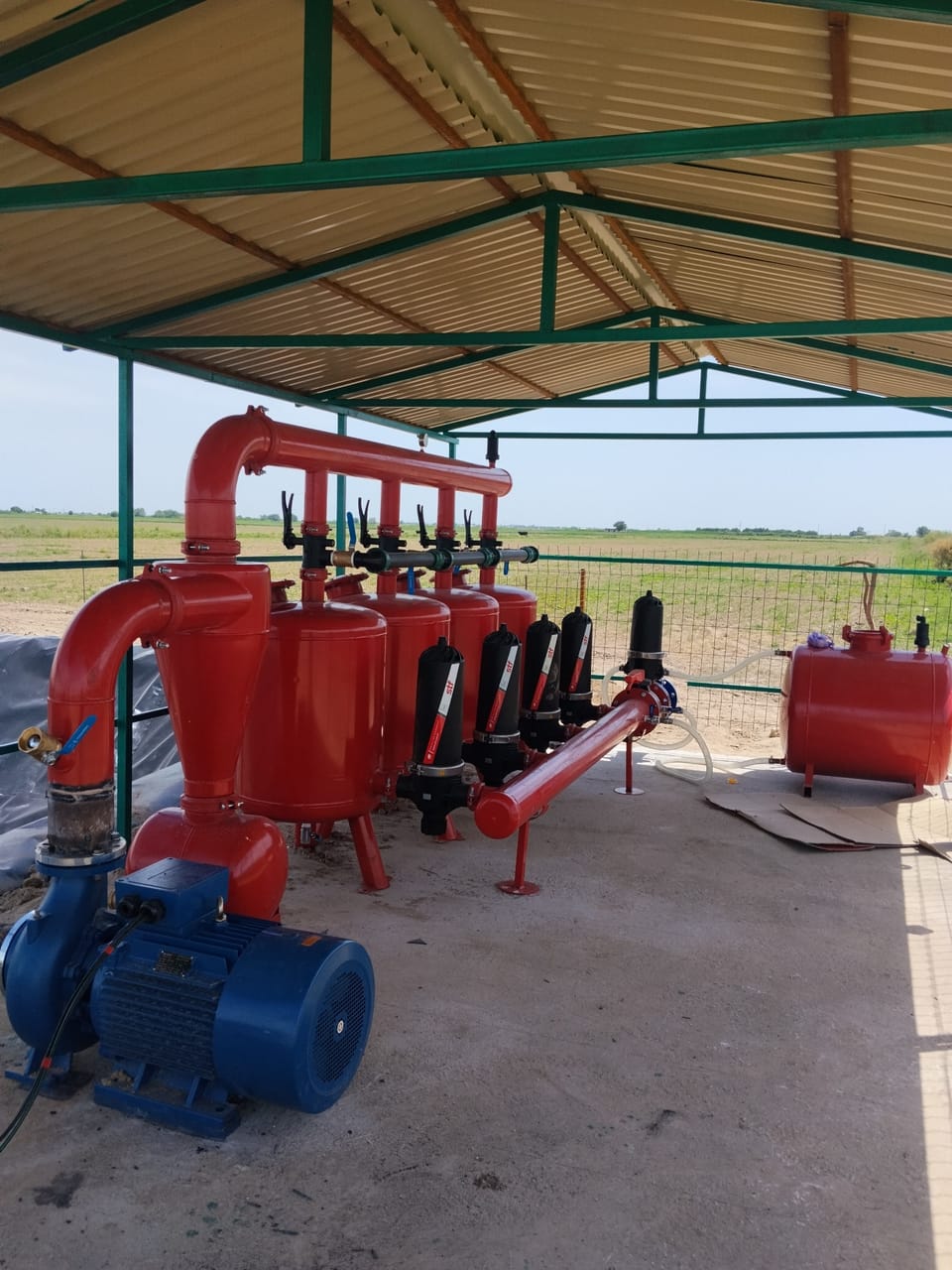 Soyabon ostida: ko‘k elektr nasos, qizil gidrotsiklon va filtr idishi, qora disk filtrlar qatori, o‘ng tomonda o‘g‘it baki.